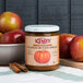 A jar of Kime's Pumpkin Butter on a table with apples and a bowl.