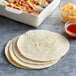 A white casserole dish with a stack of Father Sam's flour tortillas next to a bowl of red sauce.