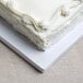 A white Enjay quarter sheet cake board under a frosted white cake.