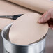 A hand using a knife to cut a circular piece of Baker's Mark PanPal liner