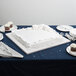 A white cake with frosting on a white Enjay square cake board on a table.