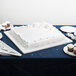A white square cake on a table with white forks and plates.