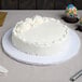 A white Enjay round cake drum under a white frosted cake on a table.