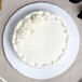 A white Enjay round cake drum under a white cake with white frosting.