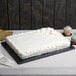 A white cake with frosting on a black Enjay half sheet cake board on a table.