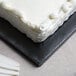 A white frosted cake on a black Enjay half sheet cake board.
