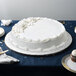 A white cake on a table with a silver round cake board underneath.