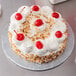 A cake with whipped cream and cherries on a silver Enjay round cake drum.