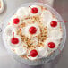 A cake on a silver round cake drum with whipped cream and cherries on top.