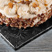 A close up of a frosted cake with pecans on a black Enjay square cake drum.