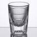 A clear Libbey fluted shot glass on a reflective surface.