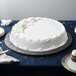 A white frosted cake on an Enjay black round cake drum on a table.