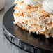 A slice of cake on an Enjay black round cake drum with white frosting and coconut flakes.