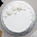 A white cake with white frosting and flowers on a silver round cake board.