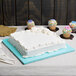 A white cake on a blue Enjay square cake drum with cupcakes and a donut on top.