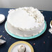 A white cake on a blue Enjay round cake drum on a table.
