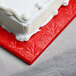 A white frosted cake on a red Enjay square cake drum.
