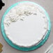 A white cake with white frosting and flowers on a blue Enjay cake drum.