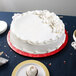 A white cake on a red Enjay cake board on a table.