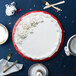 A red Enjay round cake drum under a cake with white frosting on a blue tablecloth.