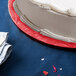 A white cake on a red Enjay round cake drum on a blue surface.