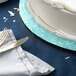 A white cake on a blue Enjay round cake drum with a knife and fork on a white tablecloth.