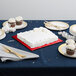 A table with a white cake on a red square cake pad and cupcakes.