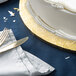 A white cake on a gold Enjay cake drum with silverware on a table.