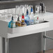 A Regency stainless steel speed rail on a counter with bottles and glasses in it.