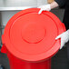 A person in gloves putting a Continental red round trash can lid on a red trash can.
