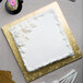 A white cake with frosting and flowers on a gold Enjay square cake drum.