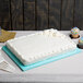 A white frosted cake on a blue Enjay fold-under cake board on a table with white plastic forks.