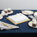 A white table set with a white cake on a gold square cake drum.