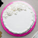 A white cake with white frosting on a pink Enjay round cake drum.