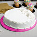 A white cake with pink frosting on a pink Enjay round cake board on a table.