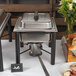 An outdoor buffet table with a Acopa wrought iron chafer stand holding a small chafing dish of food.
