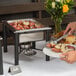 An Acopa wrought iron chafer stand holding a plate of potatoes on a buffet table.