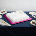 A white cake on an Enjay pink square cake drum on a table.