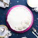 A white cake with white frosting on a pink Enjay cake drum on a blue surface with silverware.