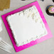 A white cake on a pink Enjay cake board with frosting on top.