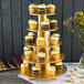 An Enjay gold cupcake stand with cupcakes decorated with frosting and sprinkles on each tier.