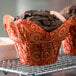 A chocolate muffin in a red Enjay Mariposa baking cup on a metal cooling rack.