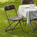 A table set with a white tablecloth and two brown Lancaster Table & Seating folding chairs on grass.