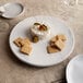 An American Metalcraft faux white marble round melamine charger with cheese and crackers on it.