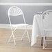 A white Lancaster Table & Seating fan back folding chair next to a table with a white tablecloth.