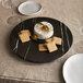 An American Metalcraft faux black marble round melamine serving board with cheese and crackers on a table.
