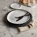 A round black marble serving board with a plate, fork, and knife on it.