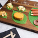A wooden cutting board with leaf cheese paper, cheese, crackers, and salami.