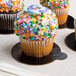 A close up of a cupcake with sprinkles on an Enjay black and gold reversible round single serve dessert board.