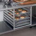 A Regency aluminum bun pan rack holding trays of bagels on a metal table.